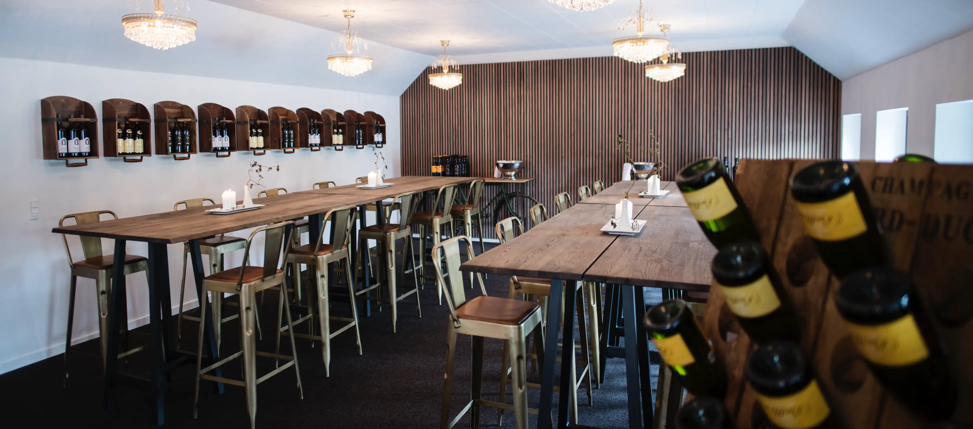 Vinbar på Venge Kloster med høje borde og vinflasker i forgrunden.