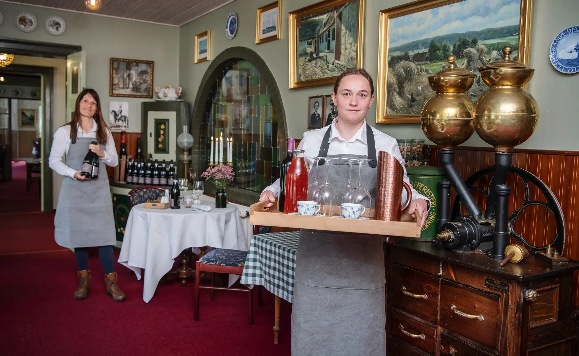 To medarbejdere med glas og serveringsbakke i en stue på Gammel Høver.