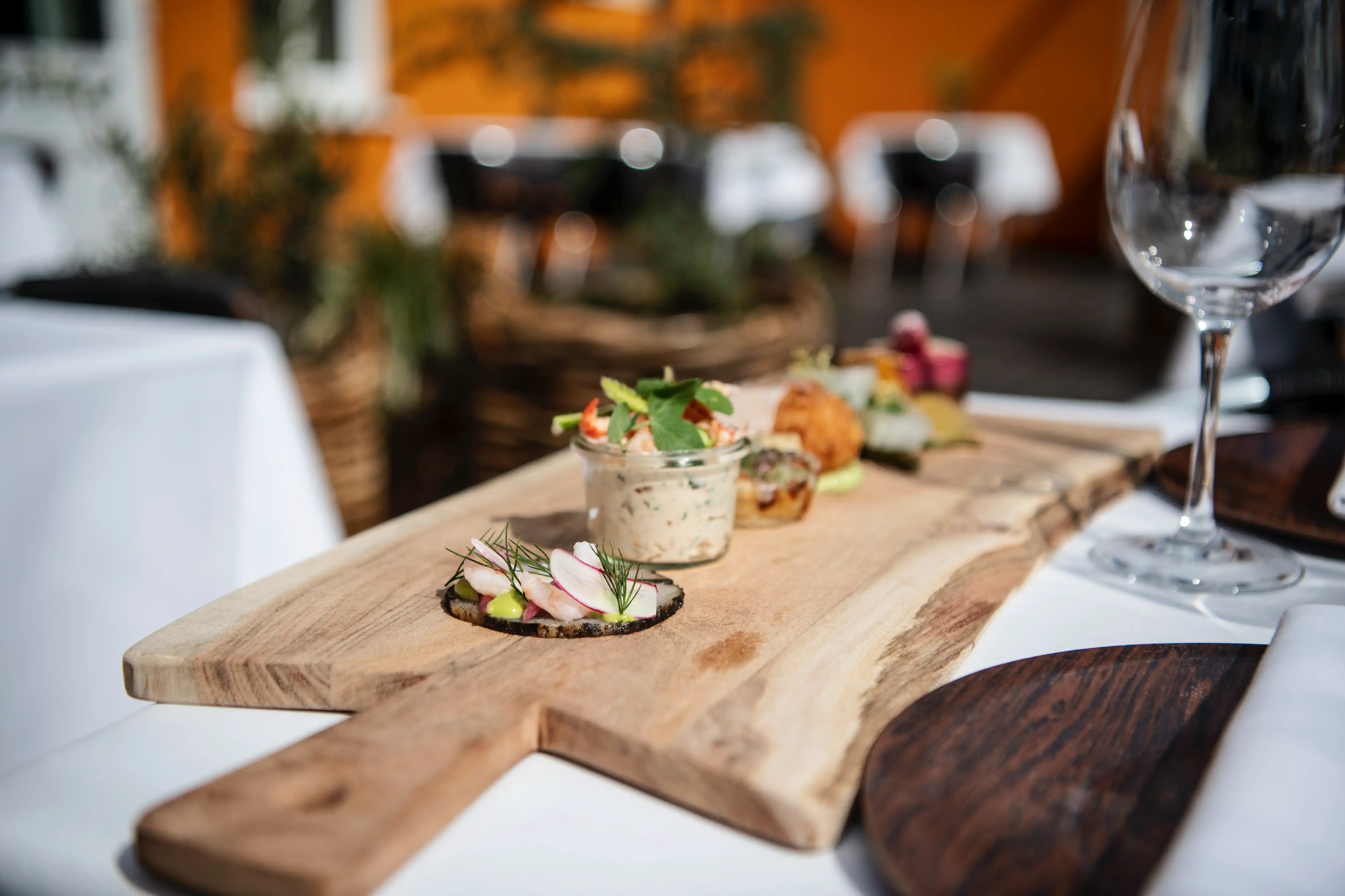 Små retter på et serveringsbræt med glas og hvide servietter på bordet.