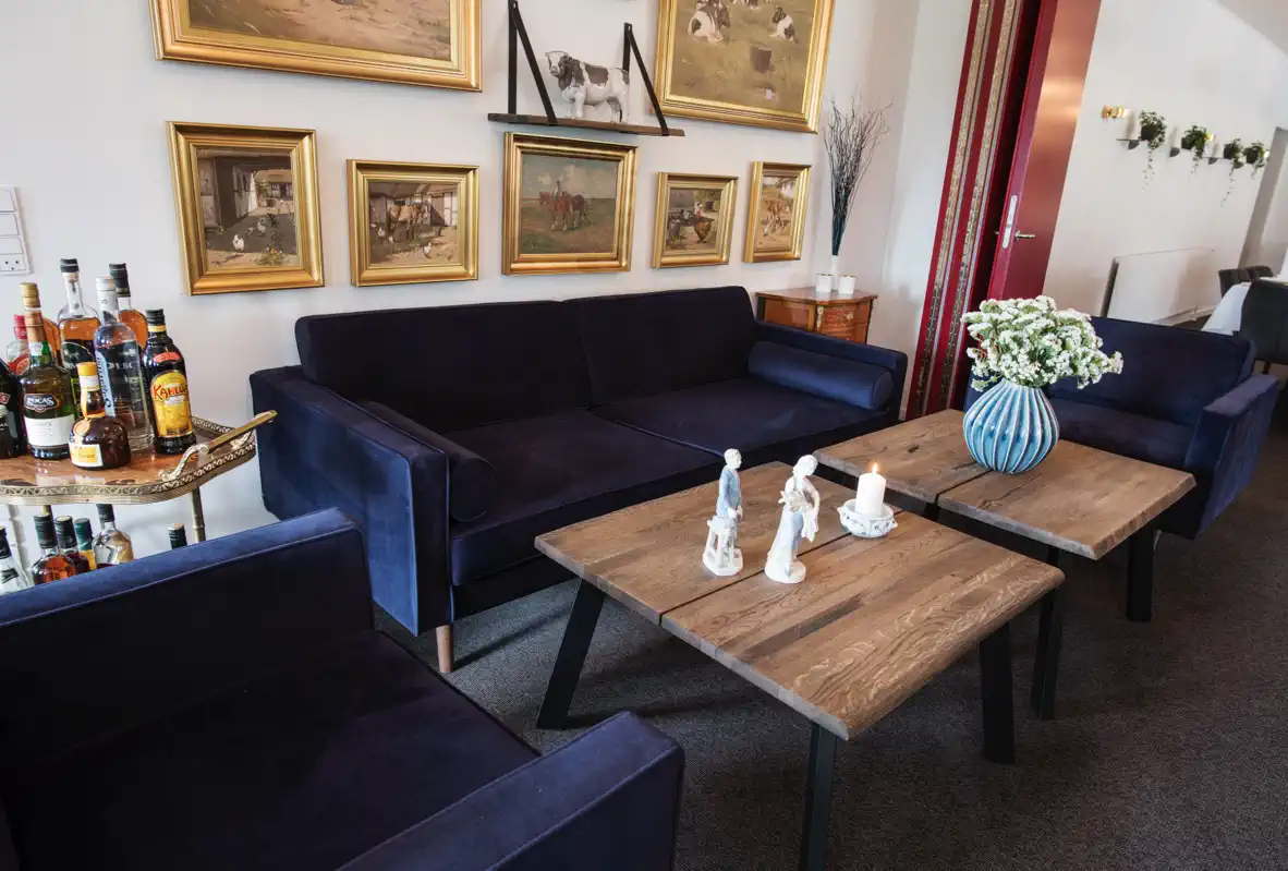 Lounge på Venge Kloster med mørkeblå sofaer, træborde og malerier.