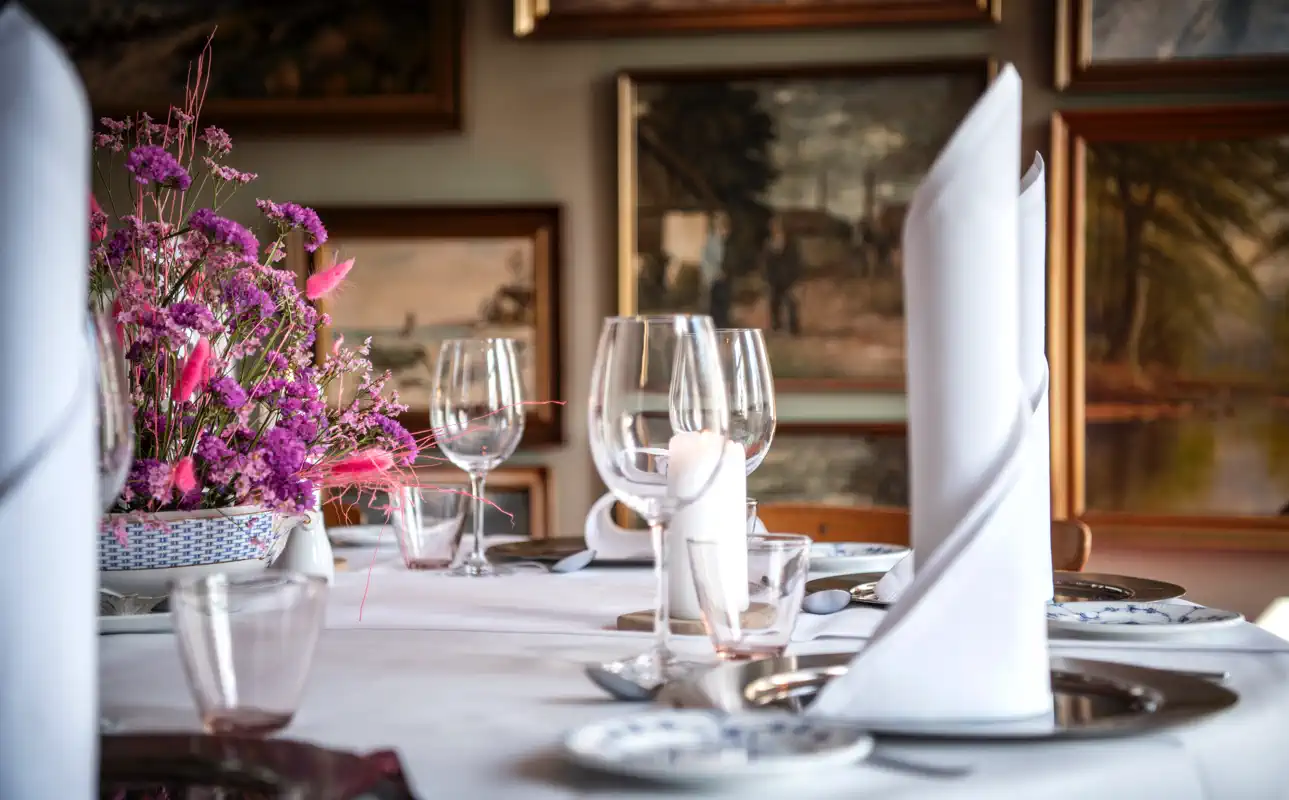 Festbord med foldede hvide servietter, vinglas og blomster.