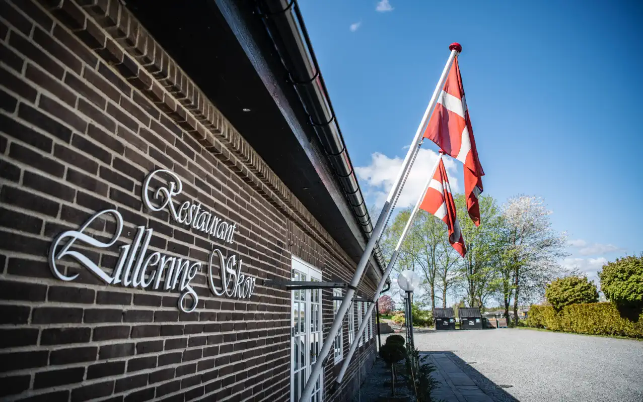 Indgangen til Lilleringskov med restaurantens navn på muren og et dansk flag.
