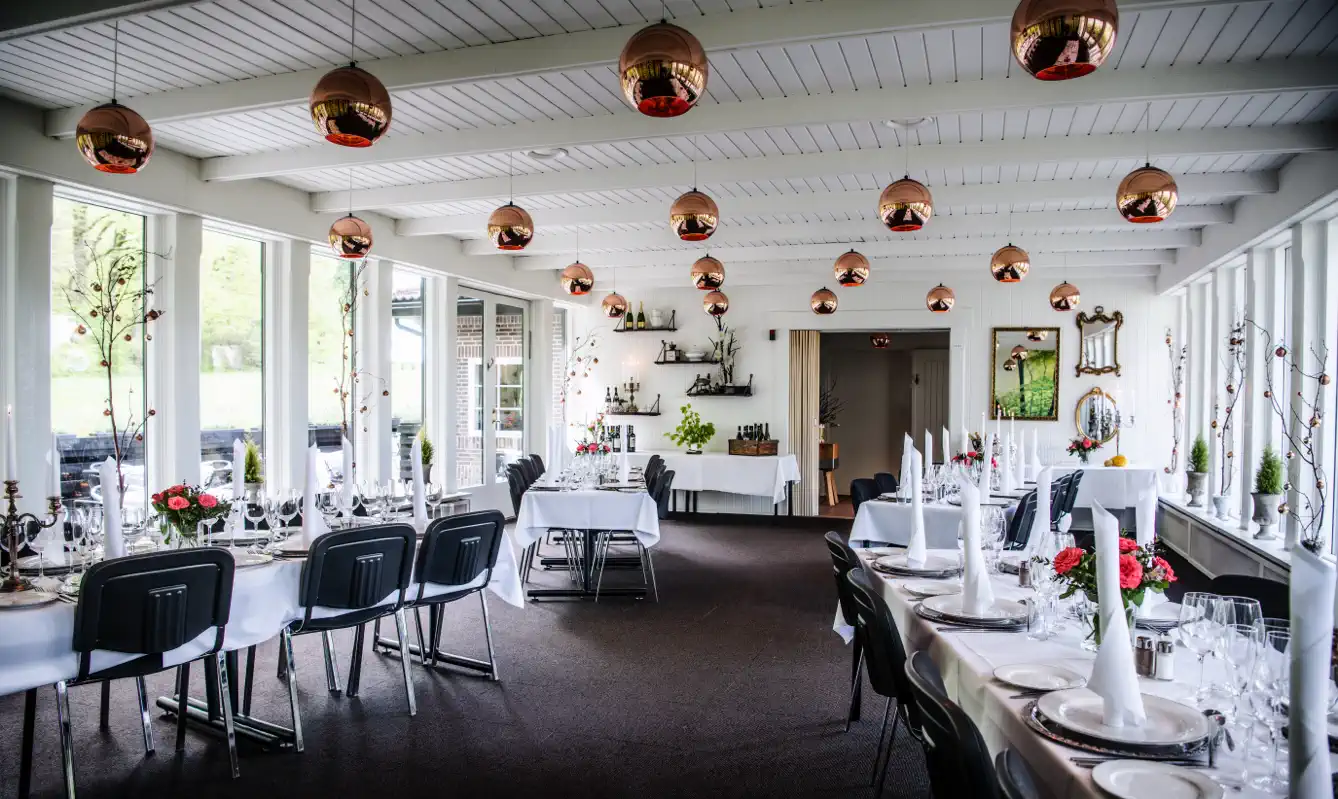 Glassalen på Lilleringskov med dækkede borde og store vinduer mod skoven.