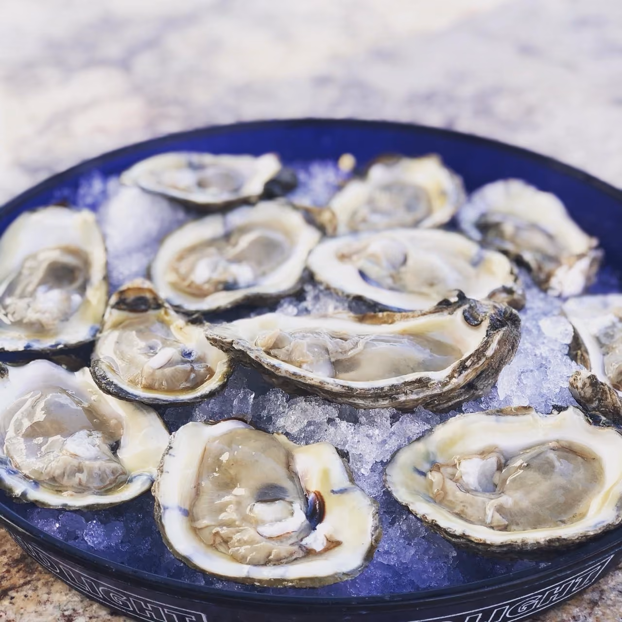 A blue tray filled with half-shell raw oysters served on crushed ice.