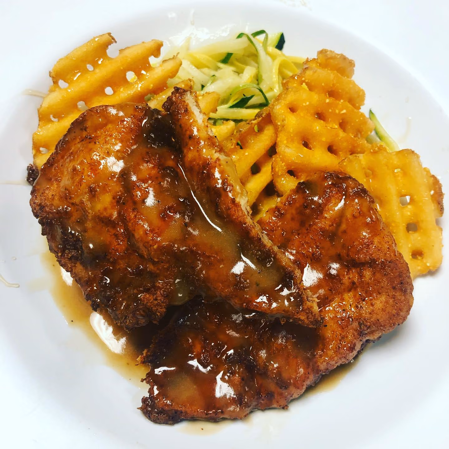 Plate with crispy, glazed grilled chicken pieces served with waffle fries and shredded zucchini.