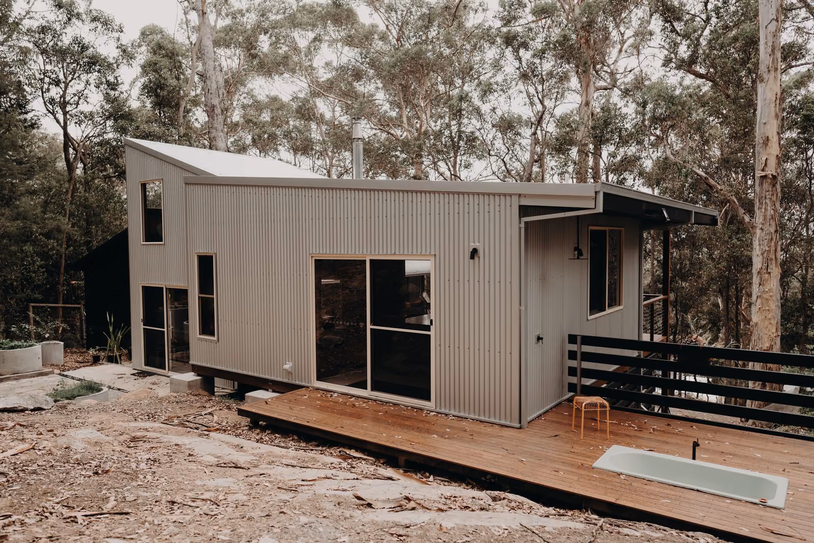 Silver corrugated steel pavilion with low timber deck set in karri bushland