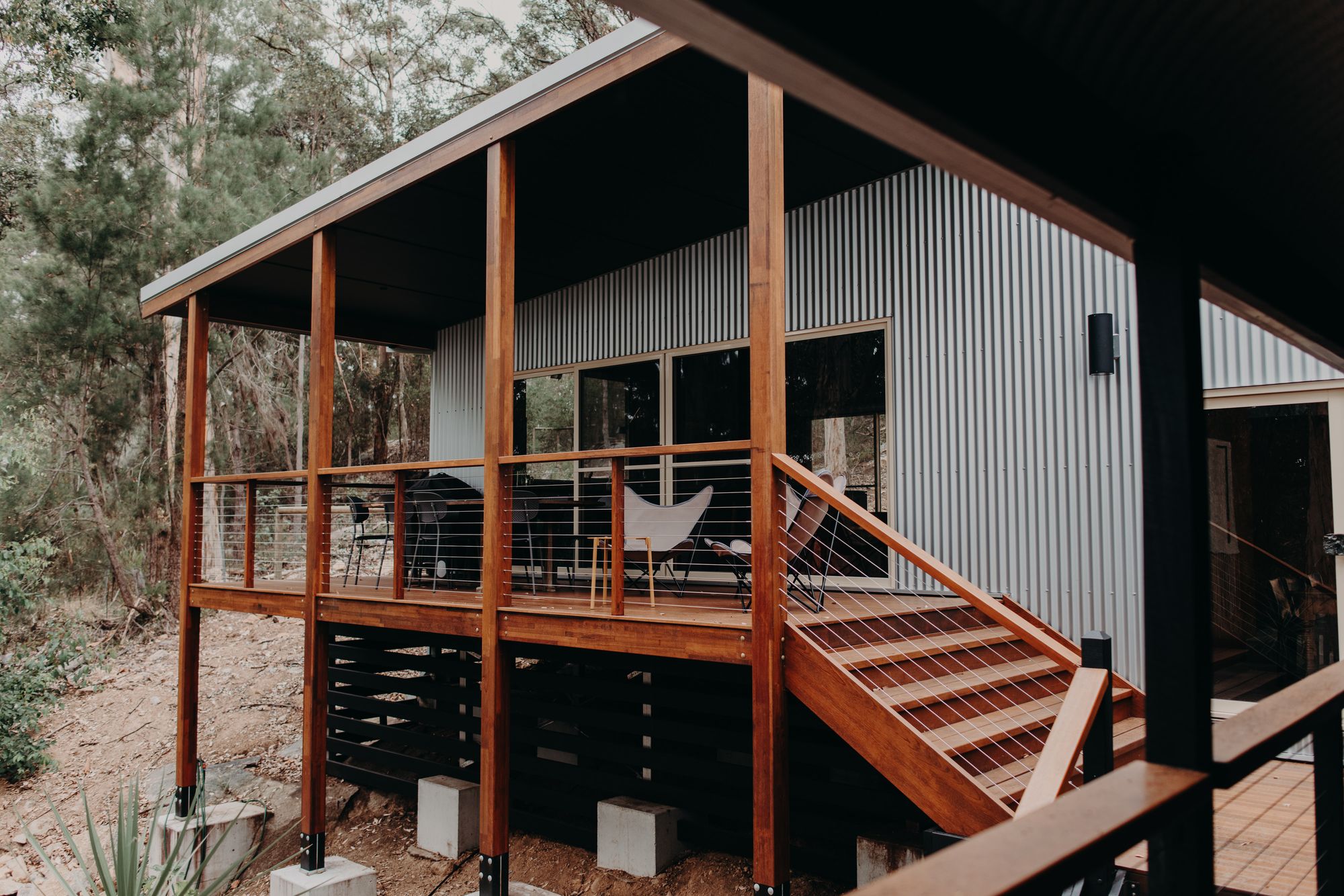 Pole home deck pavilion with timber stair, raised on posts and concrete piers over a sloping bush block in Denmark, WA