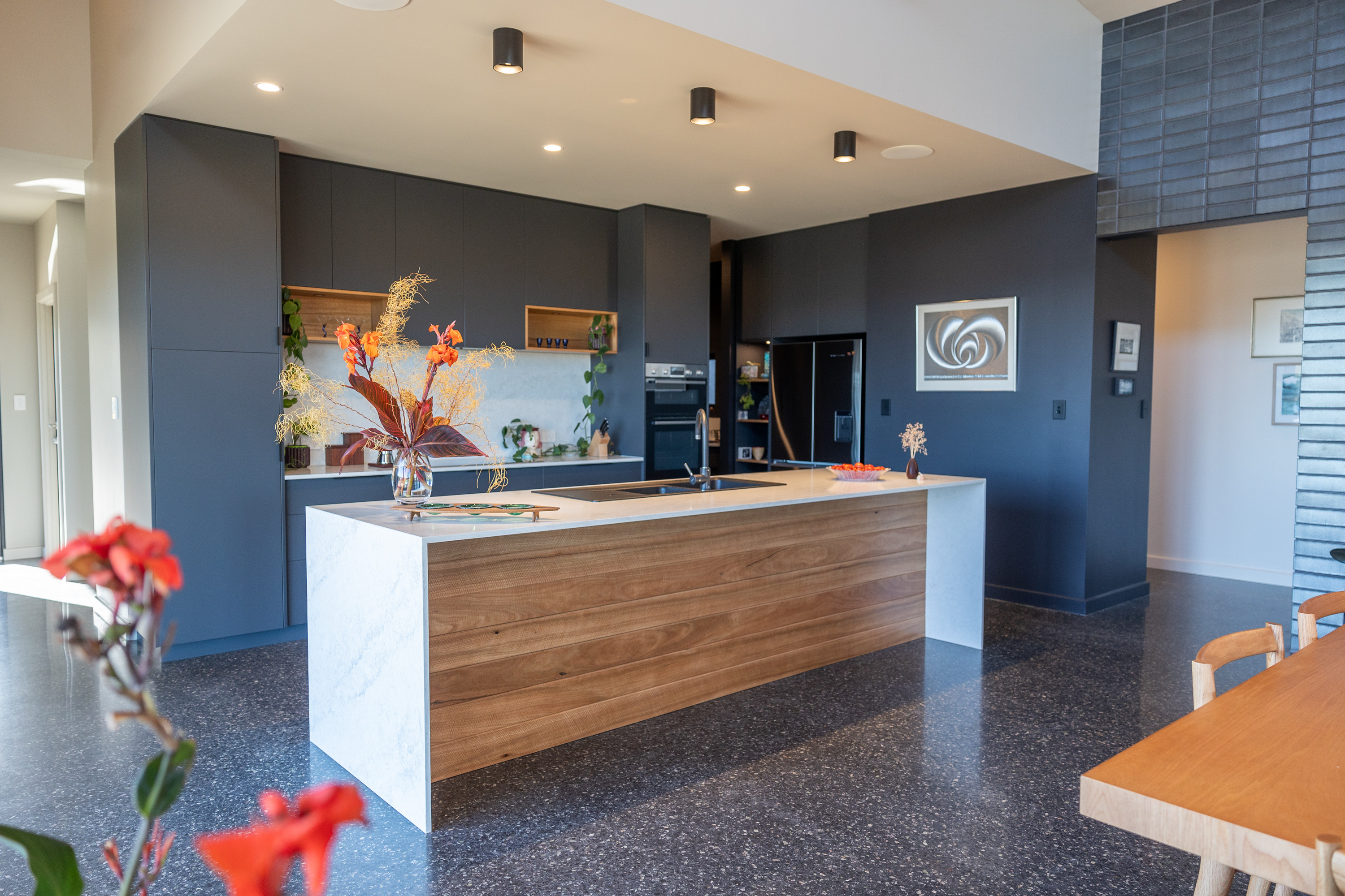 Custom kitchen with timber-clad island and charcoal joinery seen from the dining table in a Denmark, WA home