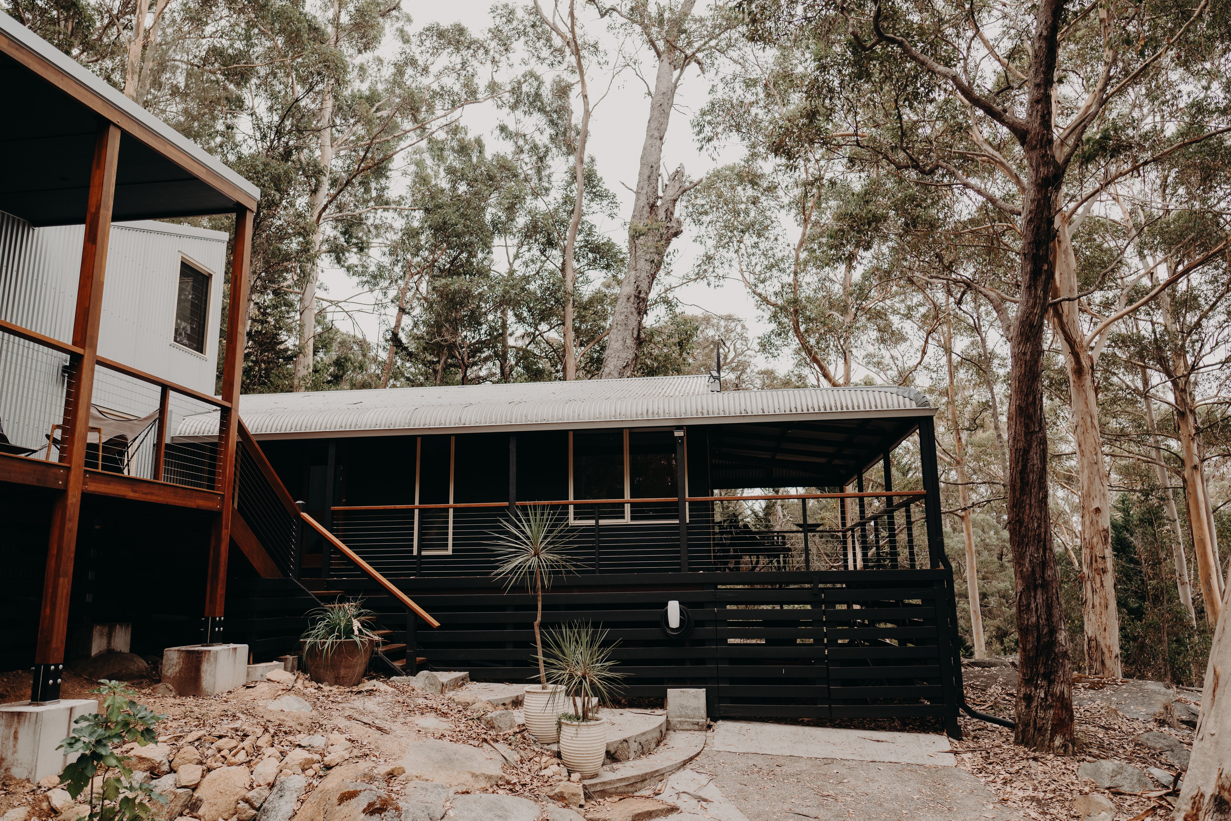 Black-clad home with a verandah among tall eucalypts and granite rocks on a bush block in Denmark, WA