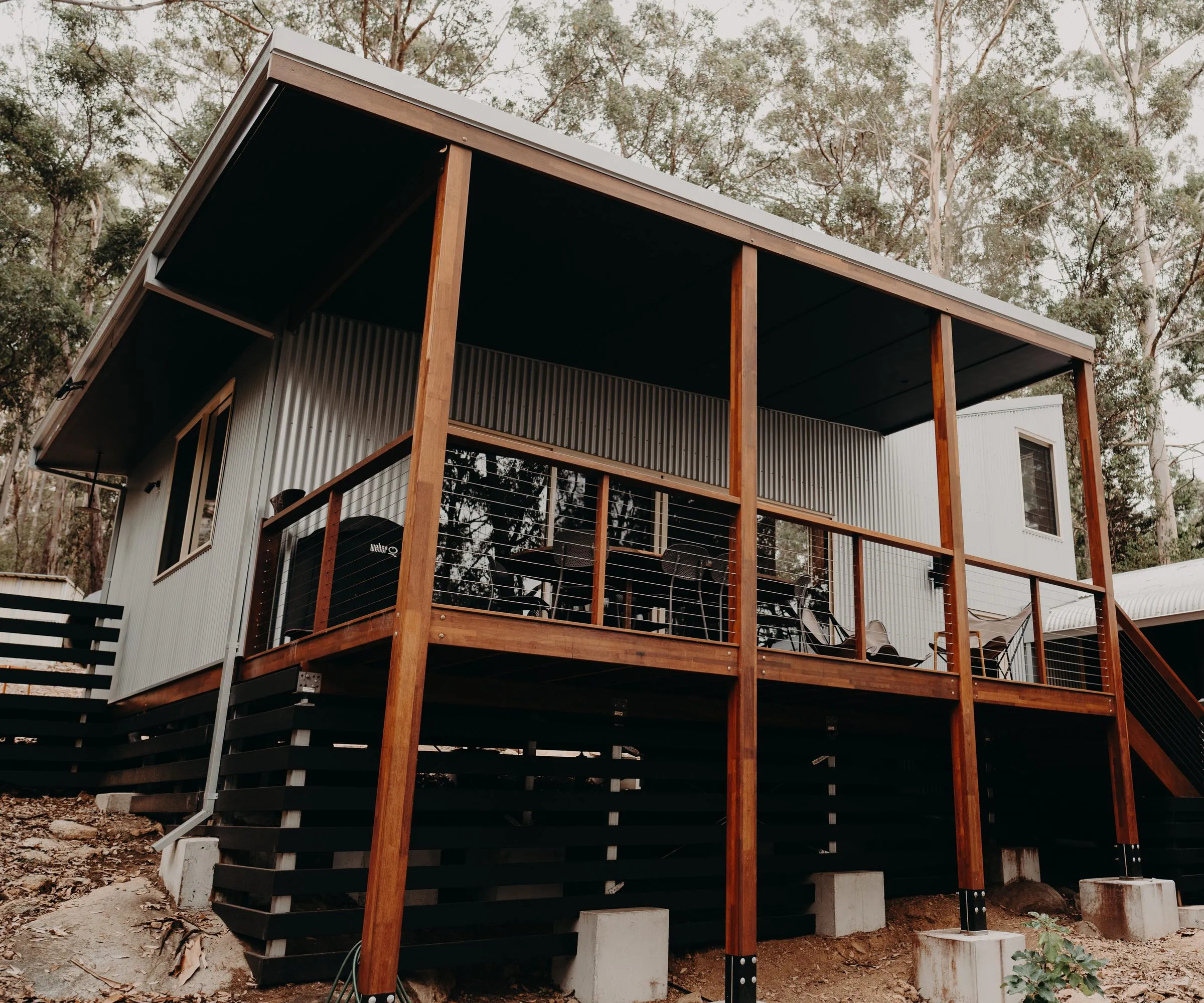 Pavilion raised on timber posts and steel stirrups over a sloping bush block
