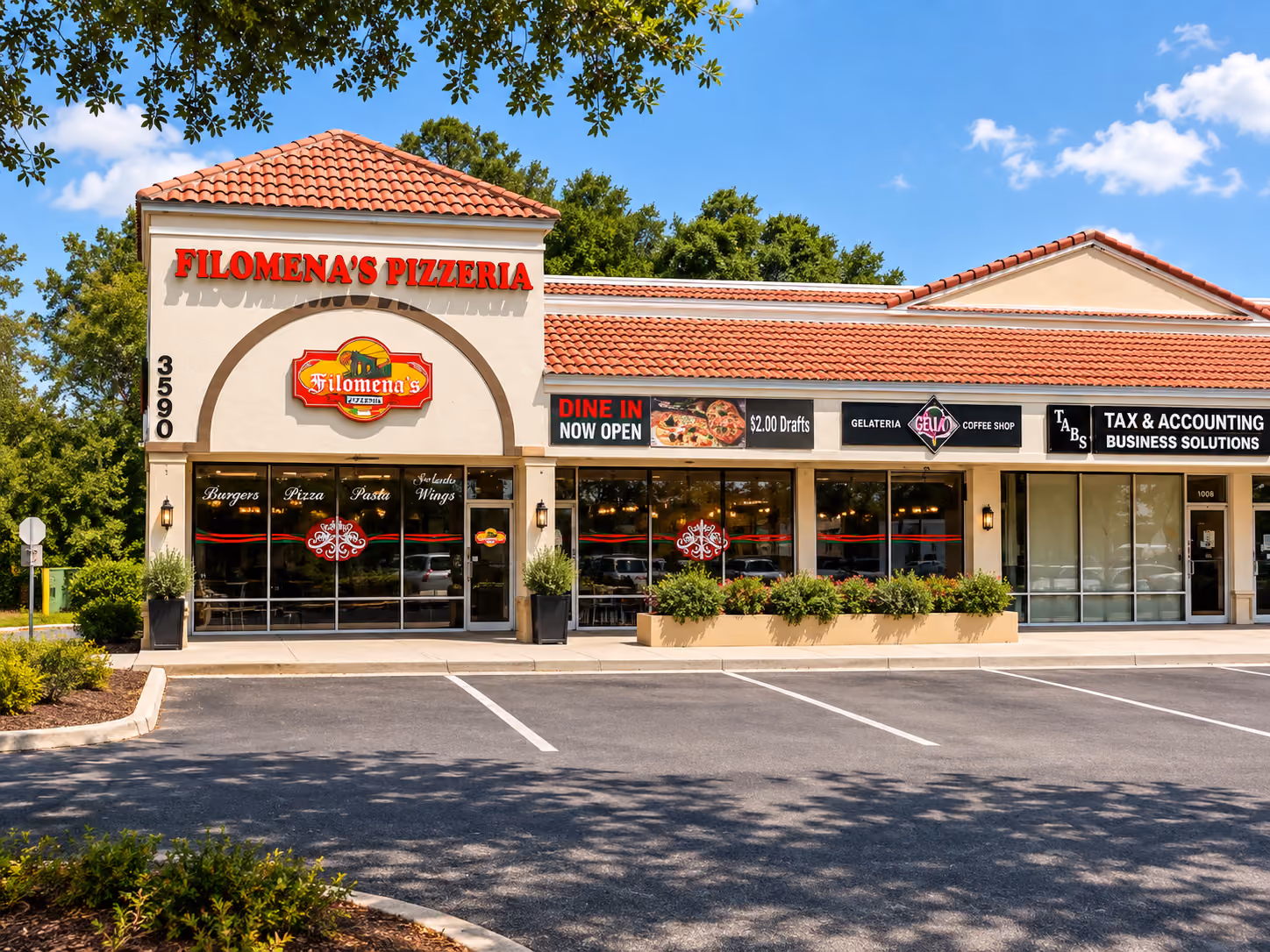 Front view of a strip mall with Filomena's Pizzeria featuring a red tiled roof and signage advertising dine-in, $2 drafts, burgers, pizza, pasta, and Orlando wings, next to Gella Gelateria coffee shop and a tax & accounting business, all under a clear blue sky with scattered clouds and some trees in the background.
