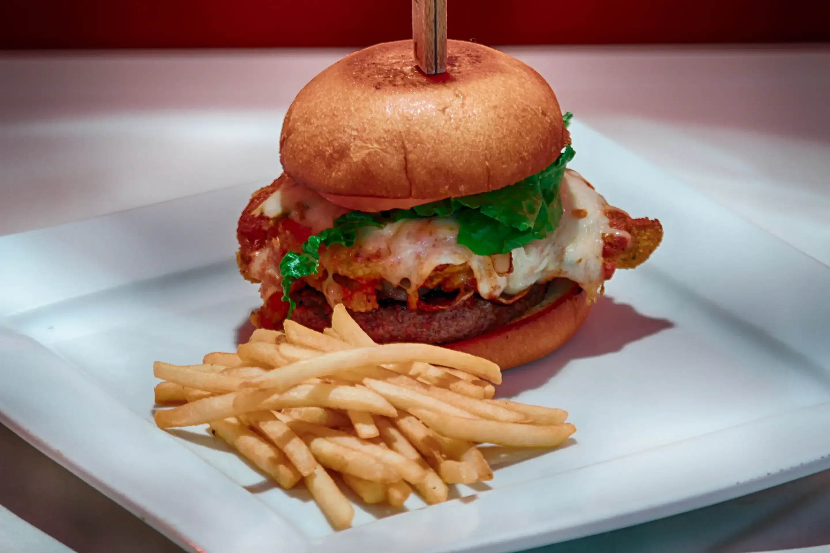 Cheeseburger with lettuce on a toasted bun, served with a side of French fries on a white square plate.