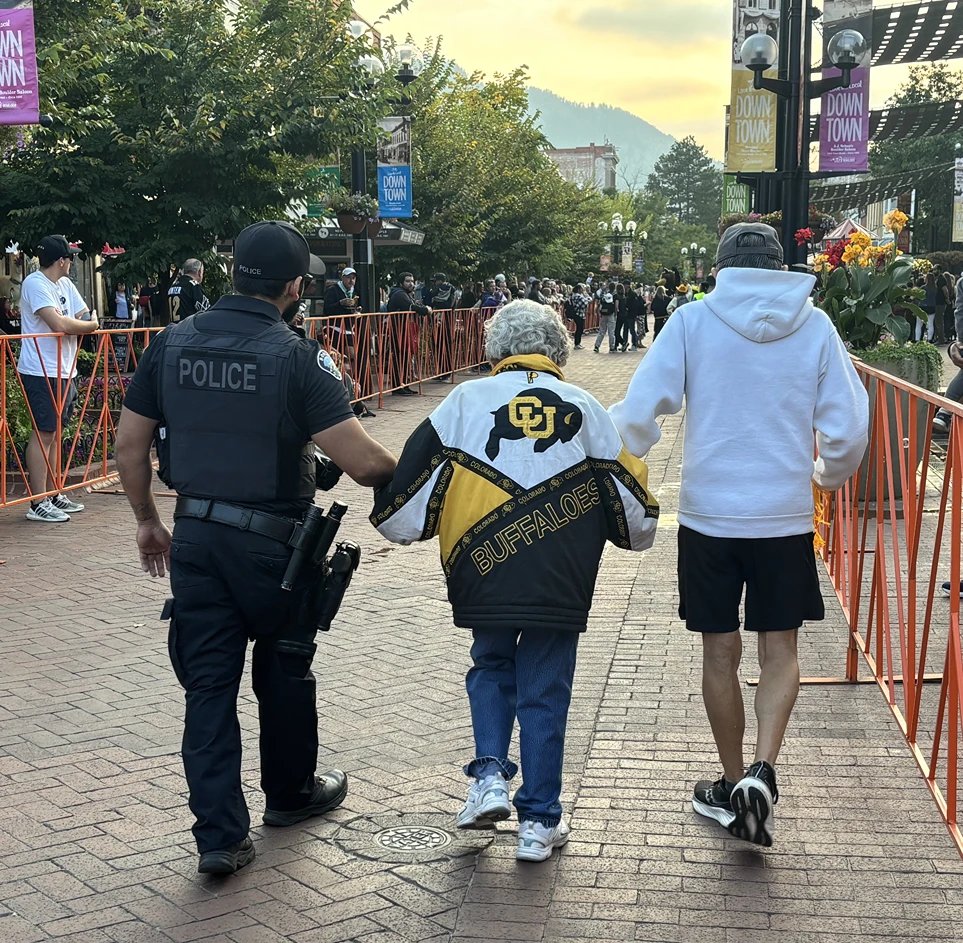 A Boulder police officer walks alongside a longtime fan on a game-day street.