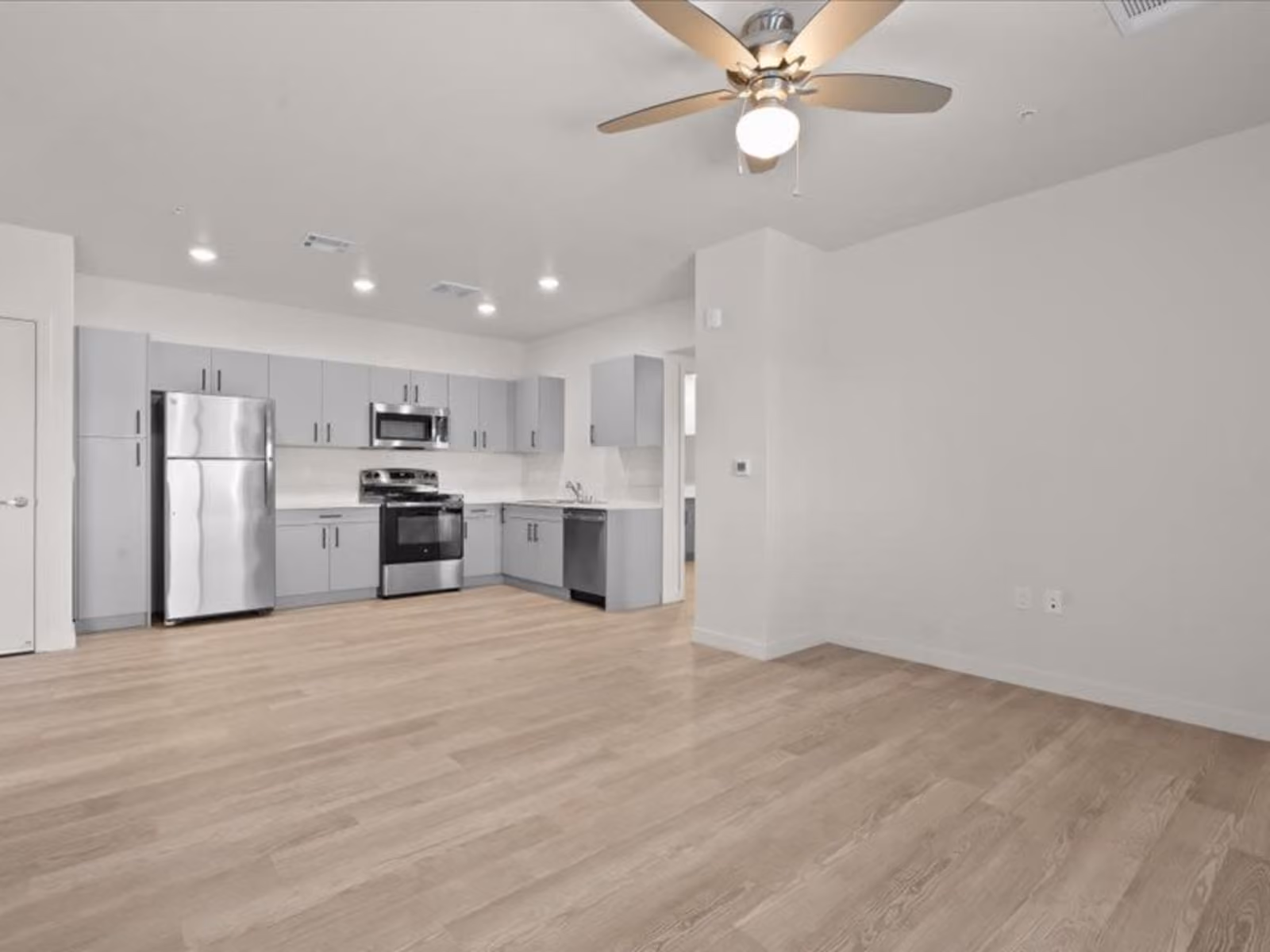 Large view of unfurnished living area and kitchen with gray cabinets and stainless steel appliances