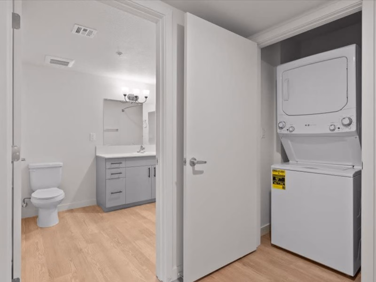 Laundry nook with stacked white appliances and view into bathroom with vanity
