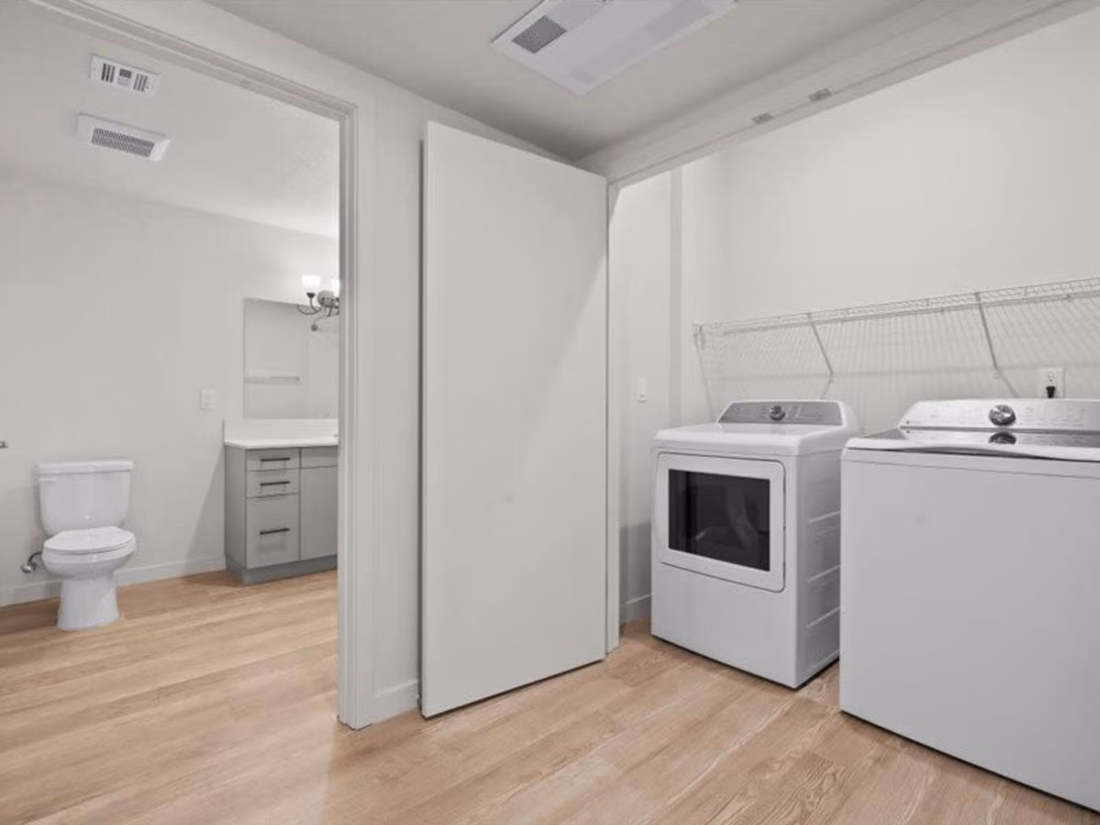 Laundry closet with white appliances and view into bathroom with vanity