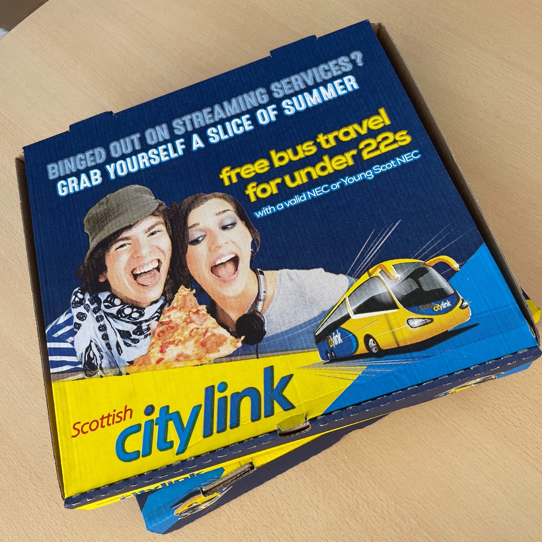 Scottish Citylink branded pizza boxes showing two young people eating pizza and promoting free bus travel for under 22s