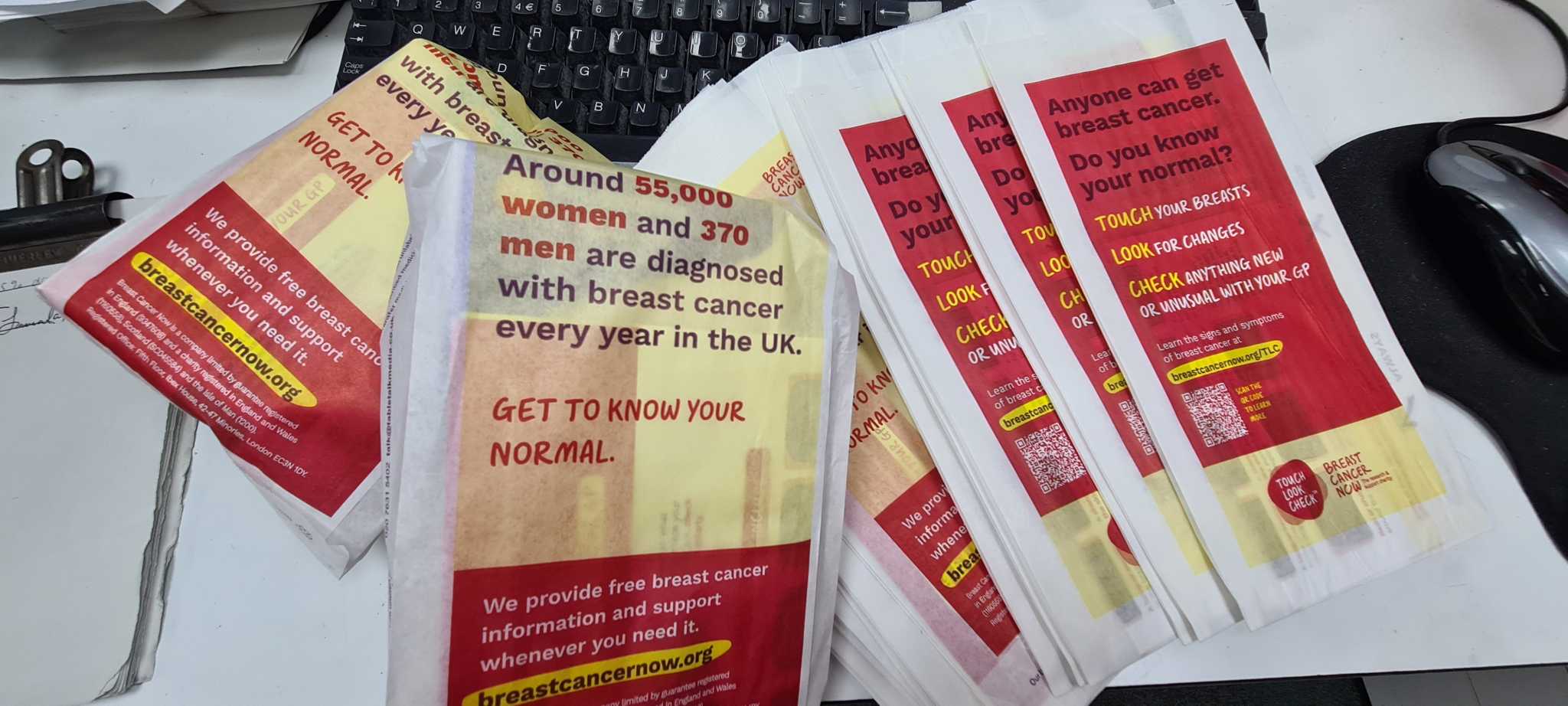 Stack of red and yellow Breast Cancer Now Touch, Look, Check pharmacy bags encouraging people to get to know their normal