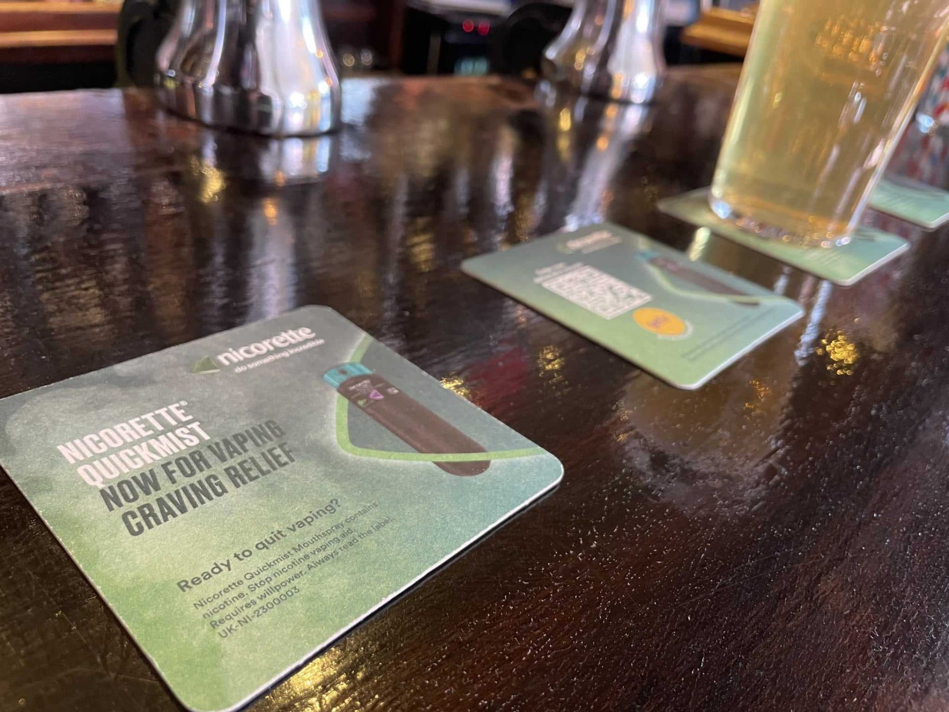 Green Nicorette QuickMist beer mats promoting vaping craving relief on a pub bar next to a pint