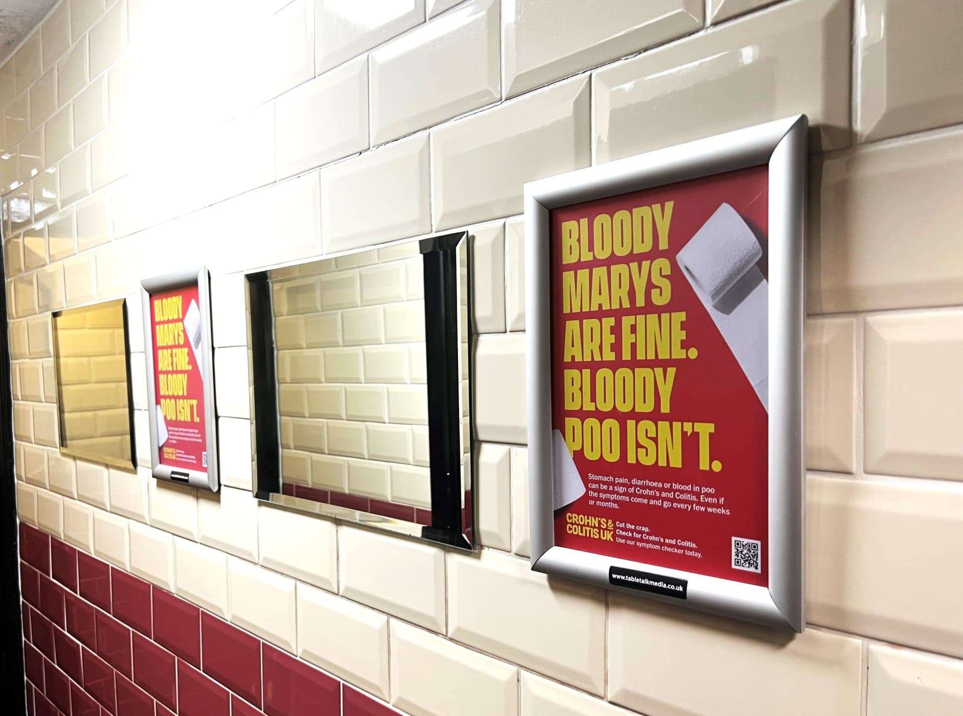Framed red Crohn's & Colitis UK posters reading 'Bloody Marys are fine. Bloody poo isn't.' on a tiled washroom wall