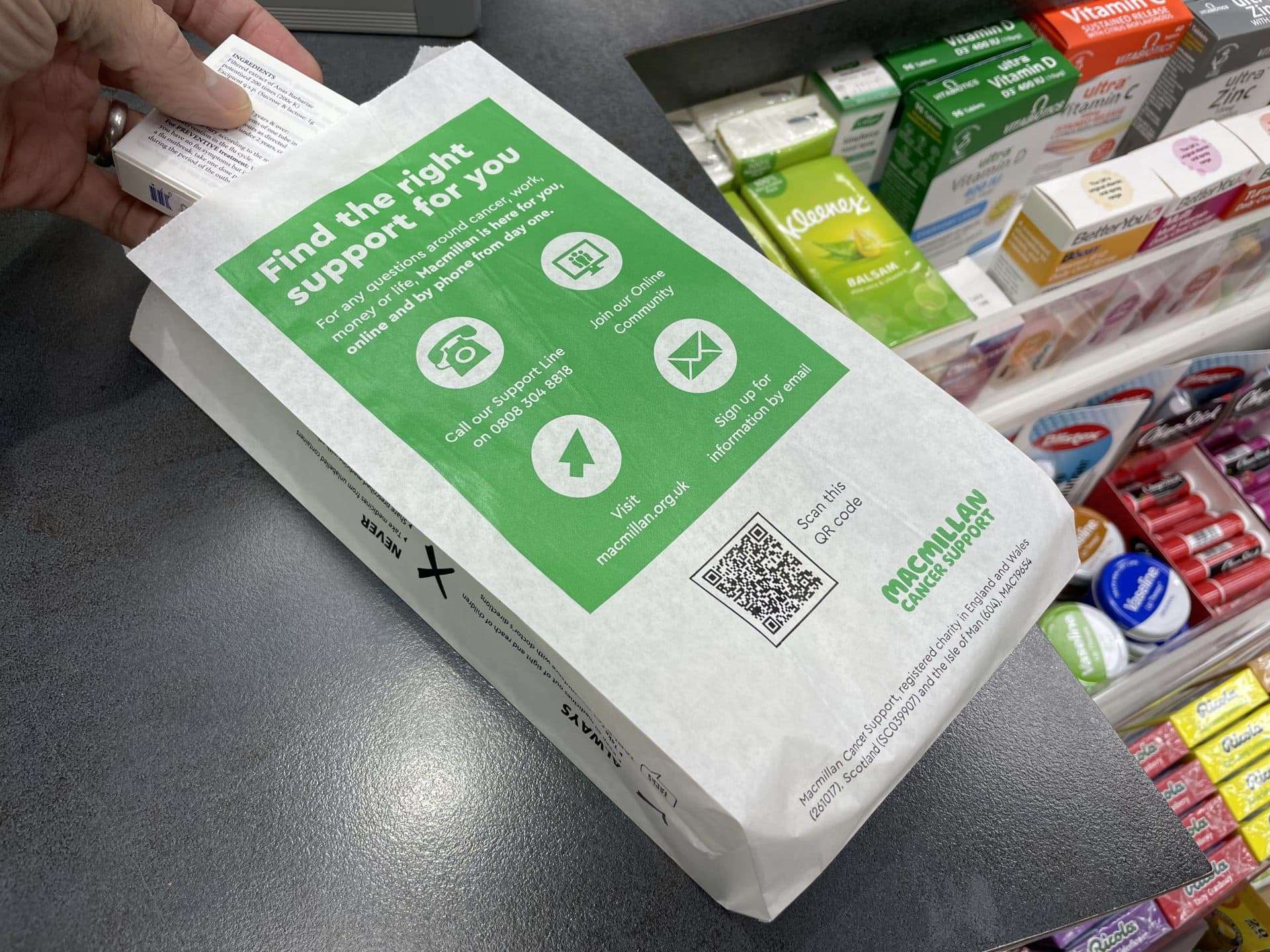 Medicine being placed into a green Macmillan Cancer Support pharmacy bag reading 'Find the right support for you', on a pharmacy counter