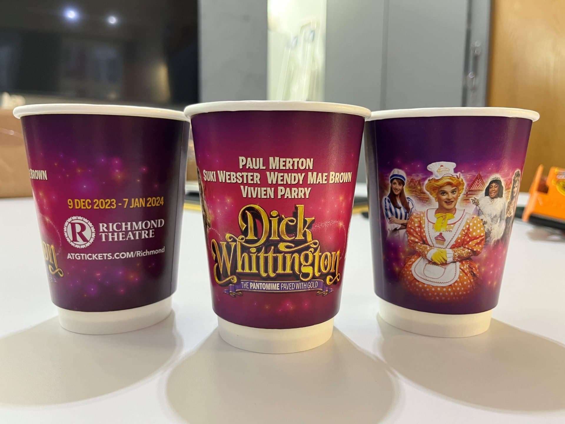 Three purple Richmond Theatre coffee cups advertising the Dick Whittington pantomime starring Paul Merton, 9 Dec 2023 to 7 Jan 2024