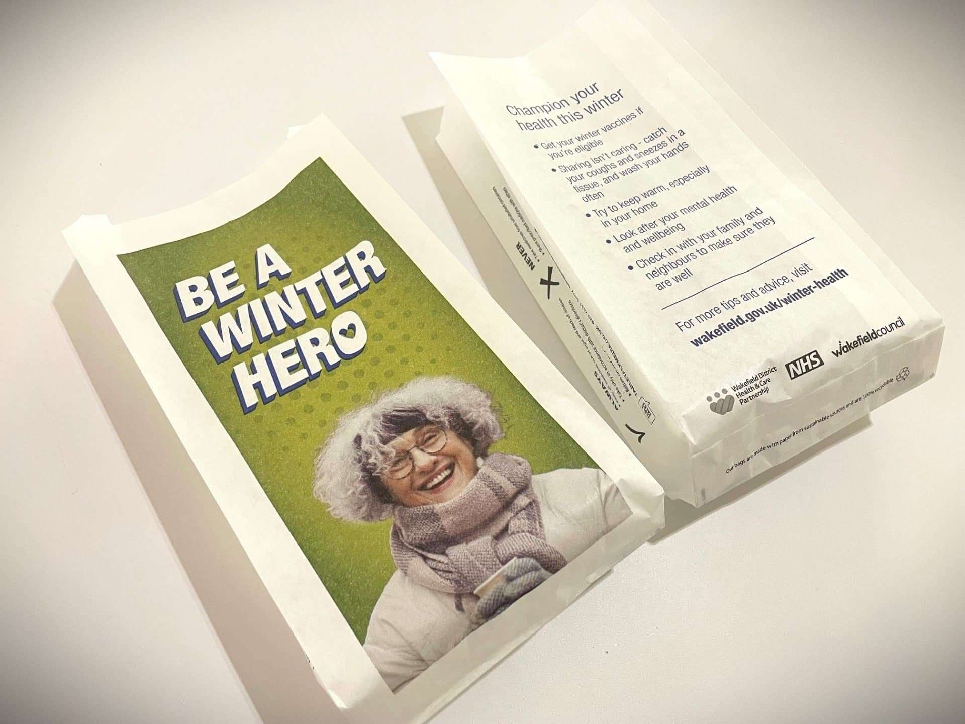 Wakefield Council and NHS pharmacy bags reading 'Be a winter hero' with a smiling older woman in a scarf, and winter health tips on the reverse