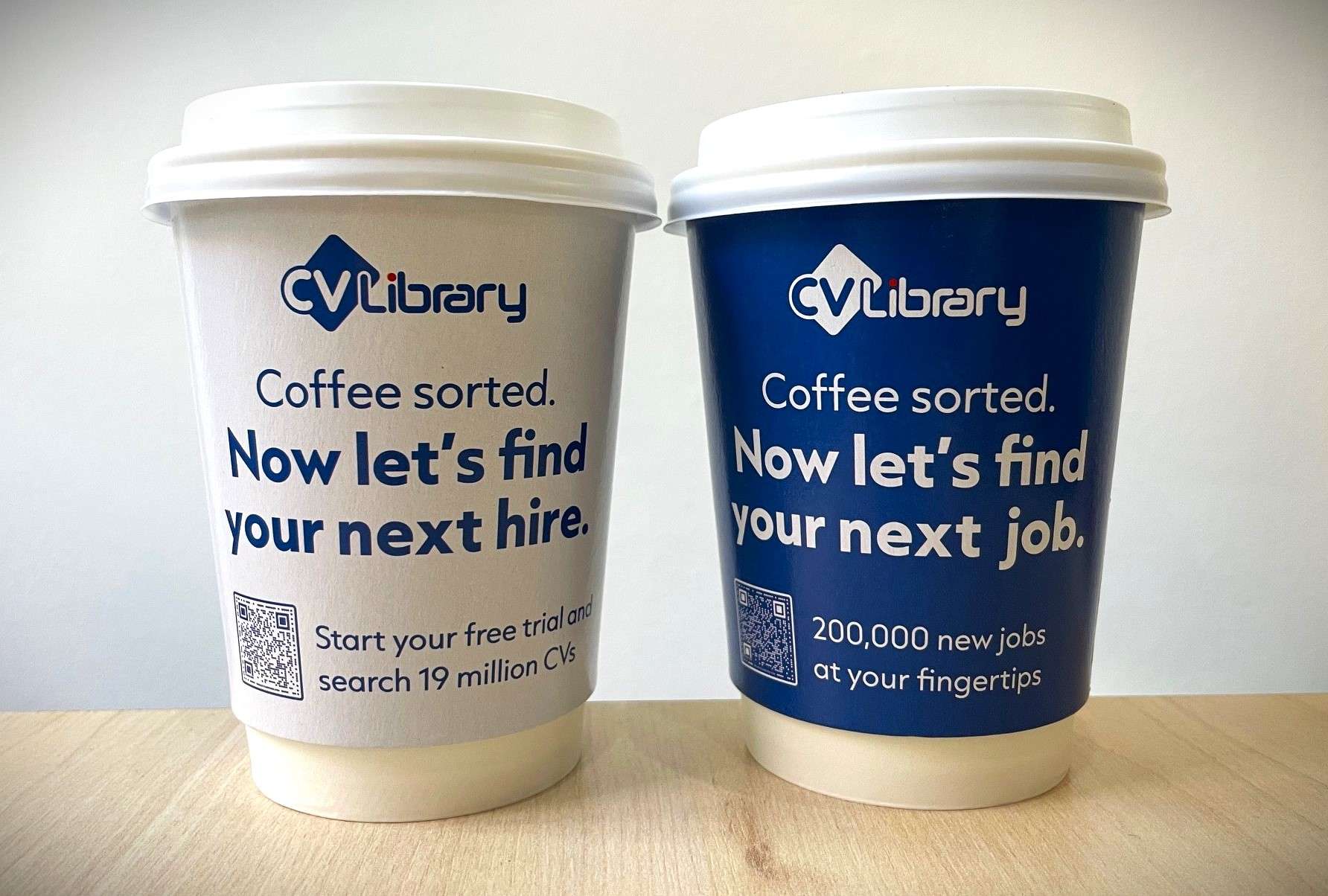 Two CV-Library coffee cups reading 'Coffee sorted. Now let's find your next hire' and 'your next job', with QR codes