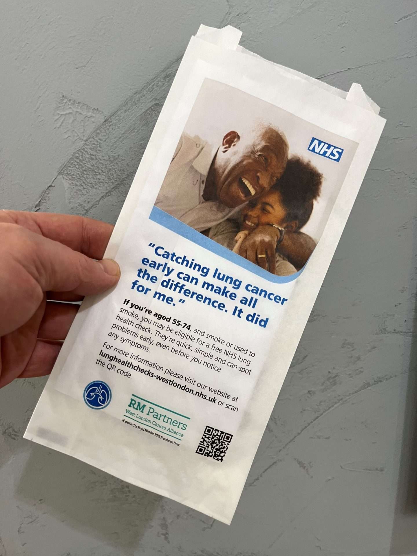 Hand holding an NHS West London lung health check pharmacy bag reading 'Catching lung cancer early can make all the difference'