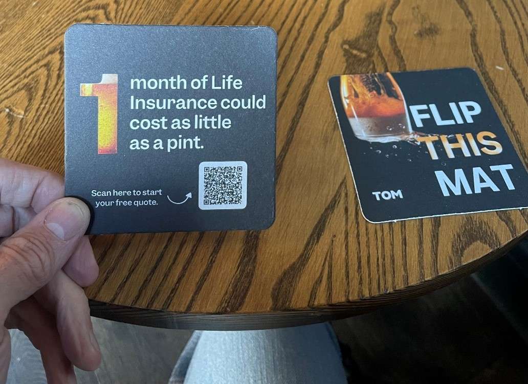 TOM life insurance beer mats reading 'Flip this mat' and '1 month of life insurance could cost as little as a pint' with a QR code, on a pub table