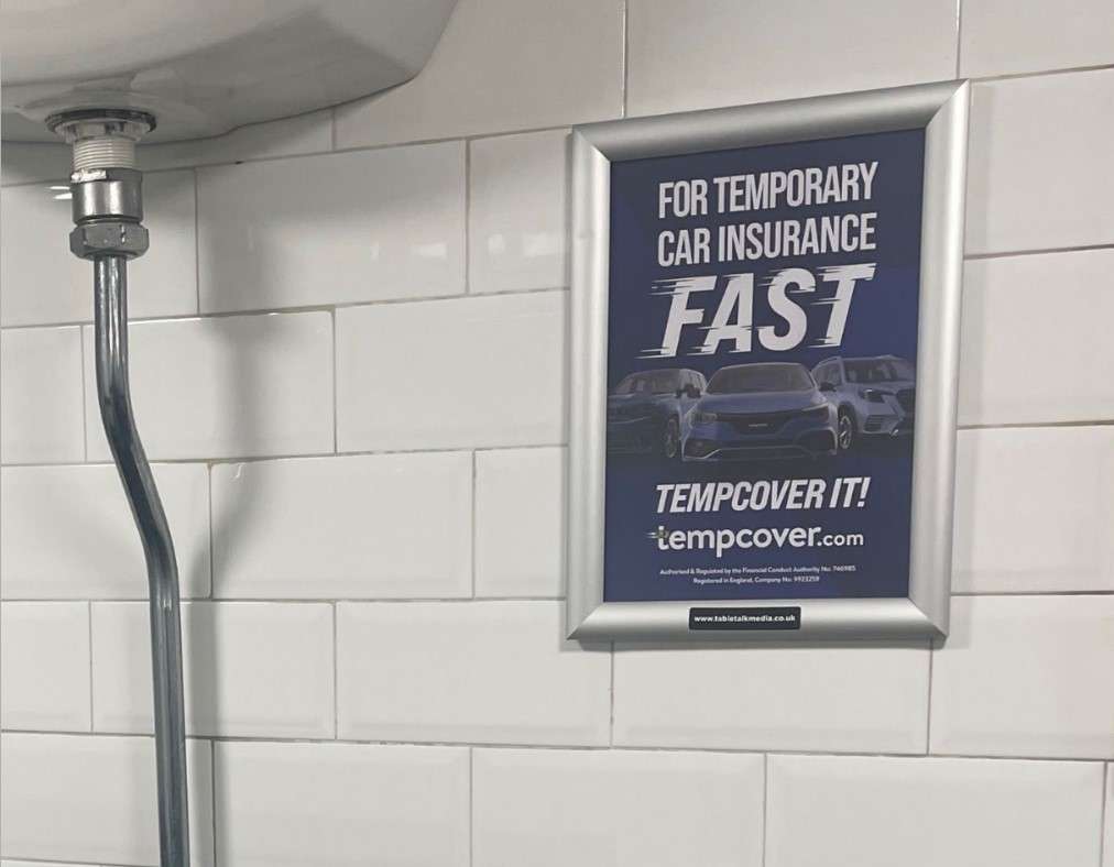 Framed Tempcover poster reading 'For temporary car insurance fast, Tempcover it!' on a tiled pub washroom wall