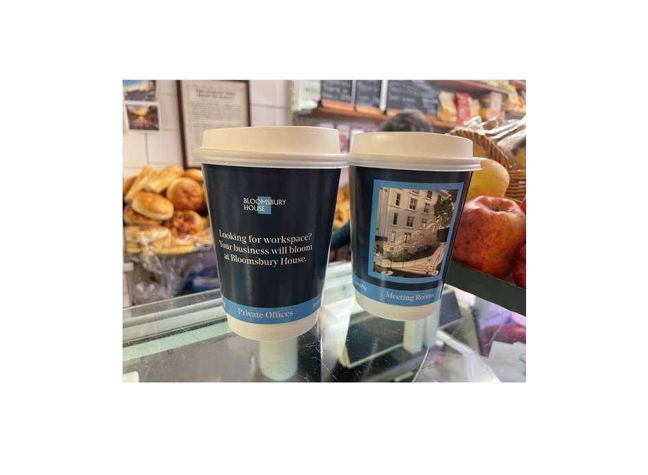 Two navy Bloomsbury House takeaway coffee cups advertising private offices and meeting rooms, on a bakery counter