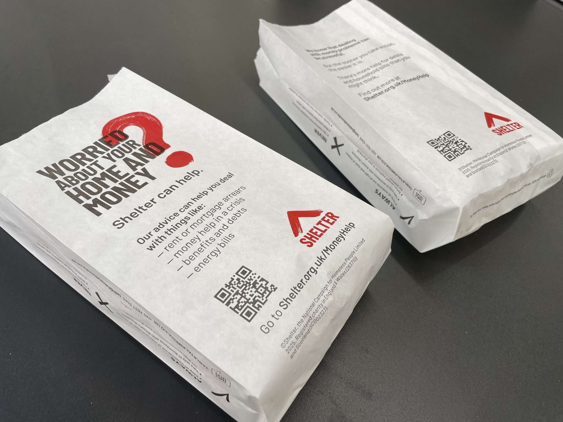 Two Shelter pharmacy bags reading 'Worried about your home and money? Shelter can help' with a QR code for money help advice