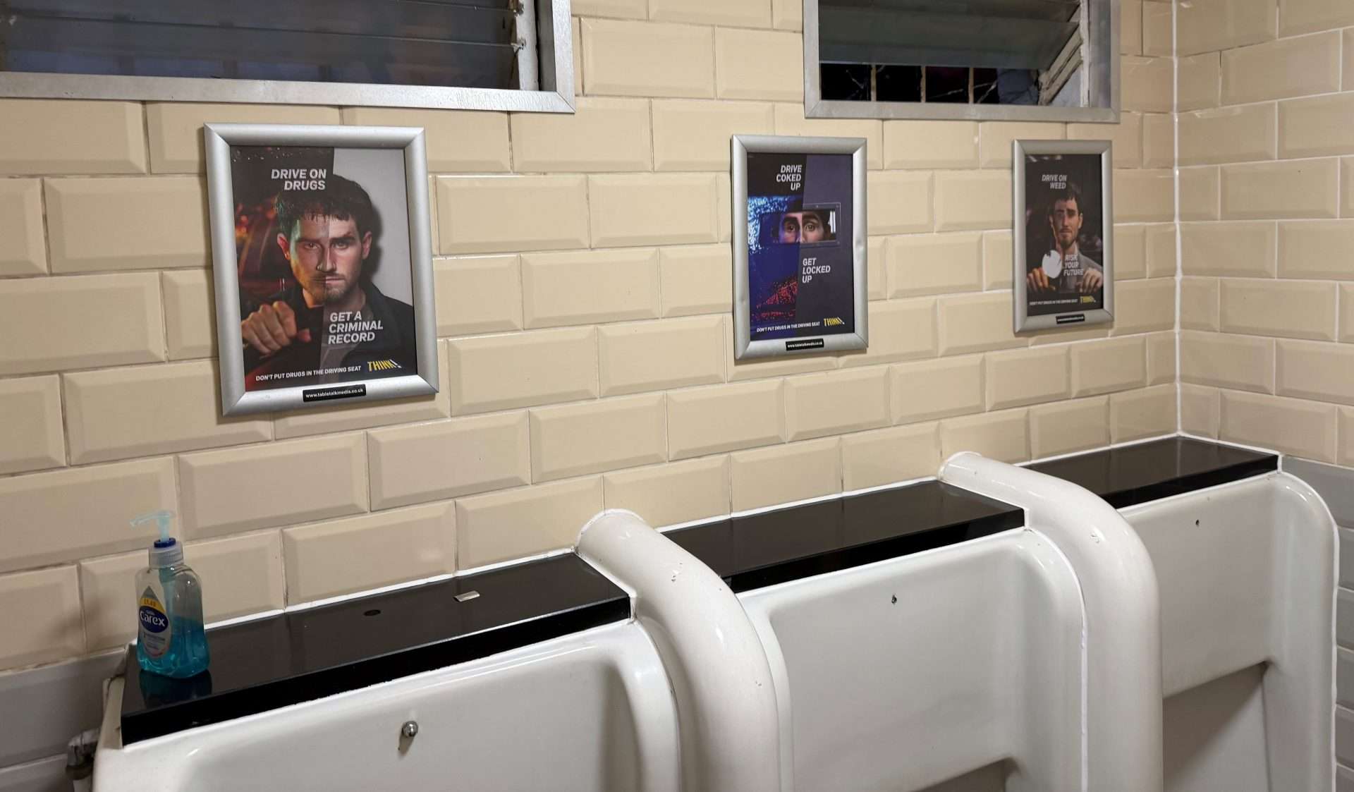 Three framed DfT THINK! drug driving posters above the urinals in a pub washroom, warning 'Drive on drugs, get a criminal record'