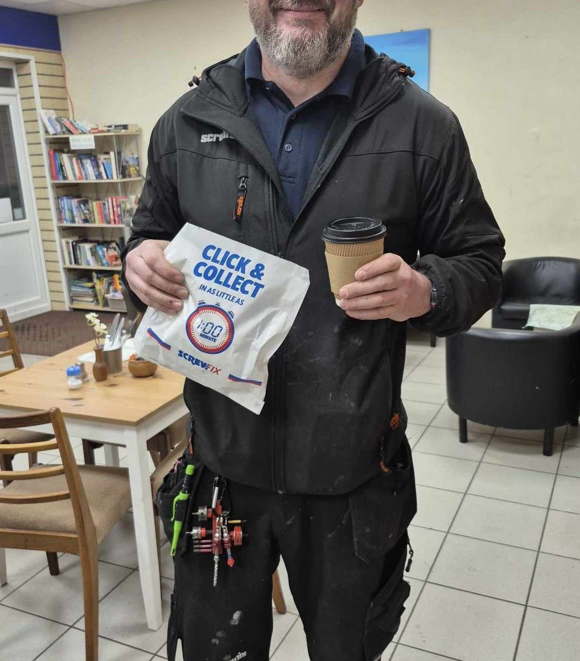 Tradesman in a cafe holding a coffee and a Screwfix Click & Collect sandwich bag