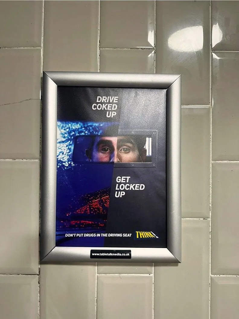THINK! 'Drive coked up, get locked up' drug-driving poster in a framed washroom panel on a white-tiled wall