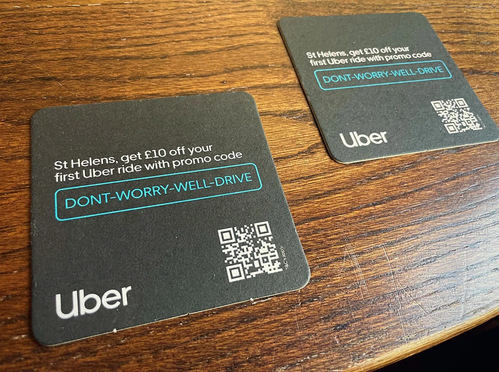 Two Uber St Helens '£10 off your first ride' promo code beer mats on a wooden pub table