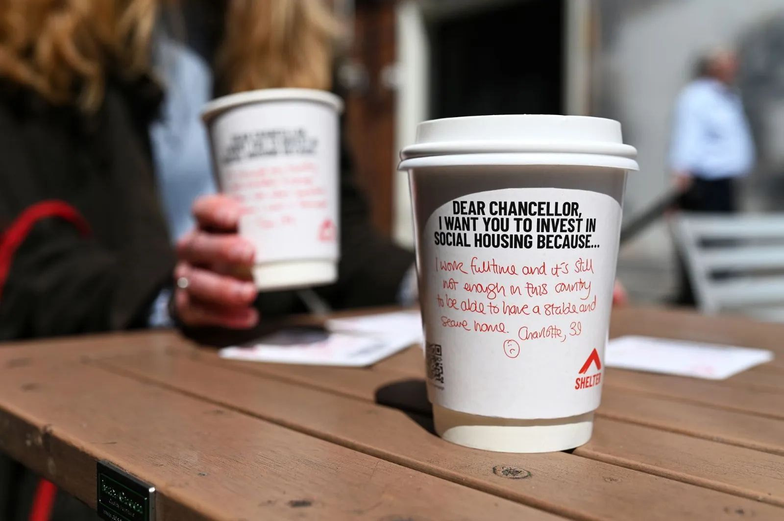 Shelter 'Dear Chancellor' social housing coffee cups with handwritten messages on an outdoor café table