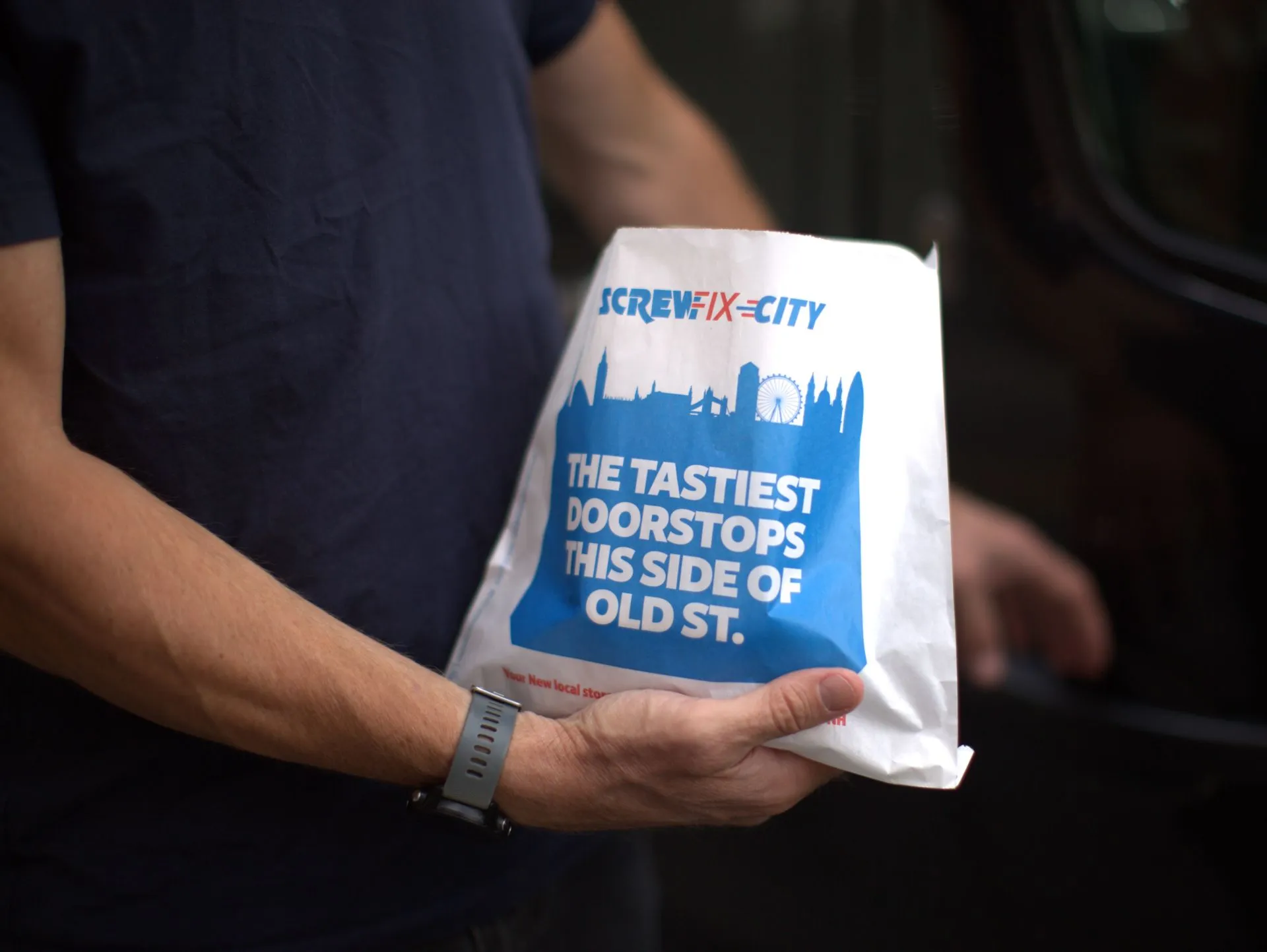 Hand holding a Screwfix City 'The tastiest doorstops this side of Old St.' sandwich bag with a London skyline