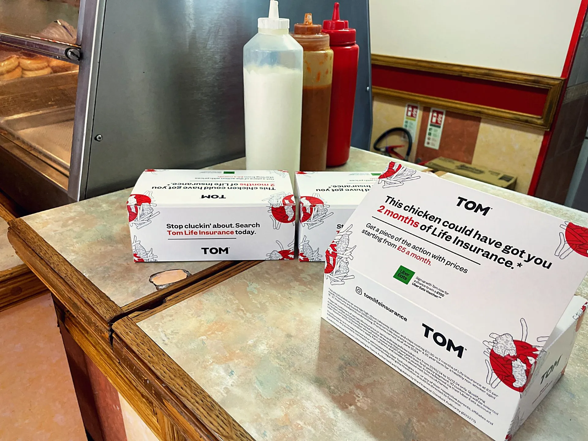 TOM Life Insurance 'This chicken could have got you 2 months of life insurance' takeaway boxes on a chicken shop counter