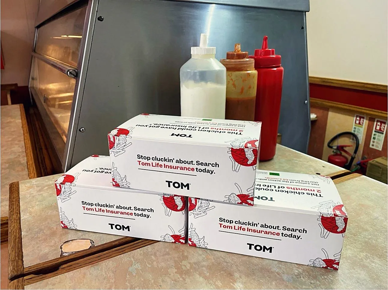 Stack of TOM Life Insurance 'Stop cluckin' about' chicken takeaway boxes on a chicken shop counter