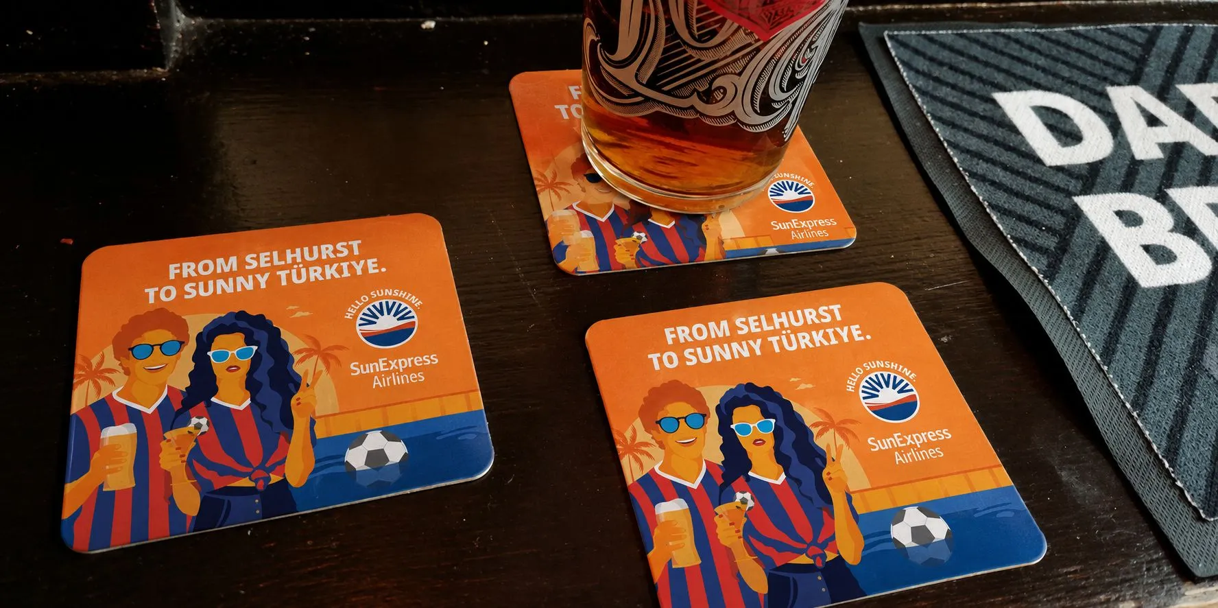 SunExpress 'From Selhurst to sunny Türkiye' beer mats on a pub table beneath a pint