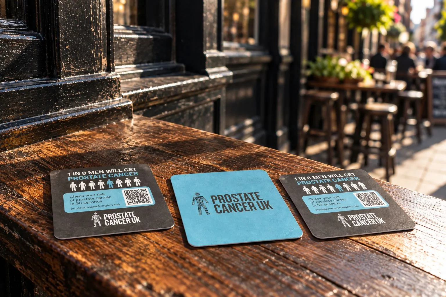 Prostate Cancer UK beer mats with QR codes on a wooden ledge outside a pub