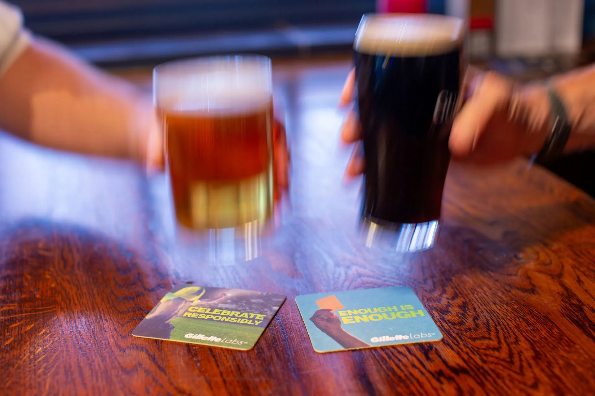Two Gillette Labs beer mats, 'Celebrate Responsibly' and 'Enough is Enough', under raised pints in a pub
