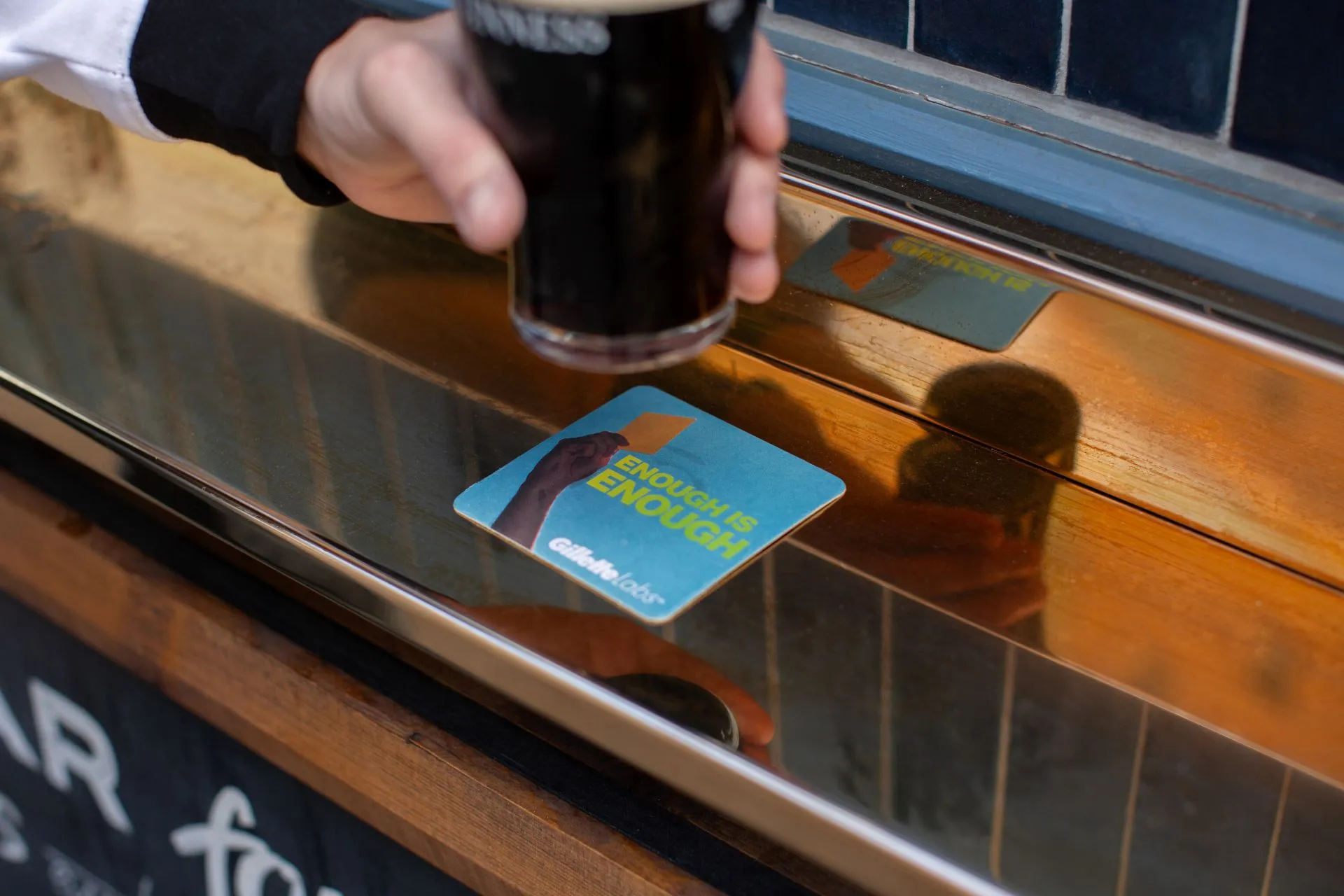 Gillette Labs 'Enough is Enough' beer mat on a pub bar as a pint of stout is lifted