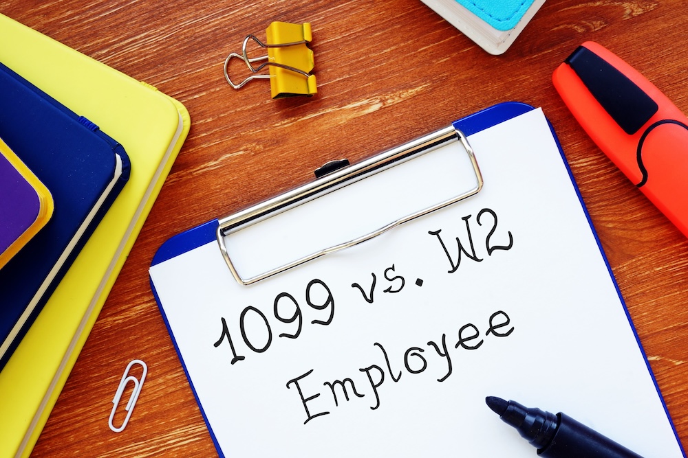 Clipboard displaying “1099 vs. W-2 Employee” on a desk with office supplies.