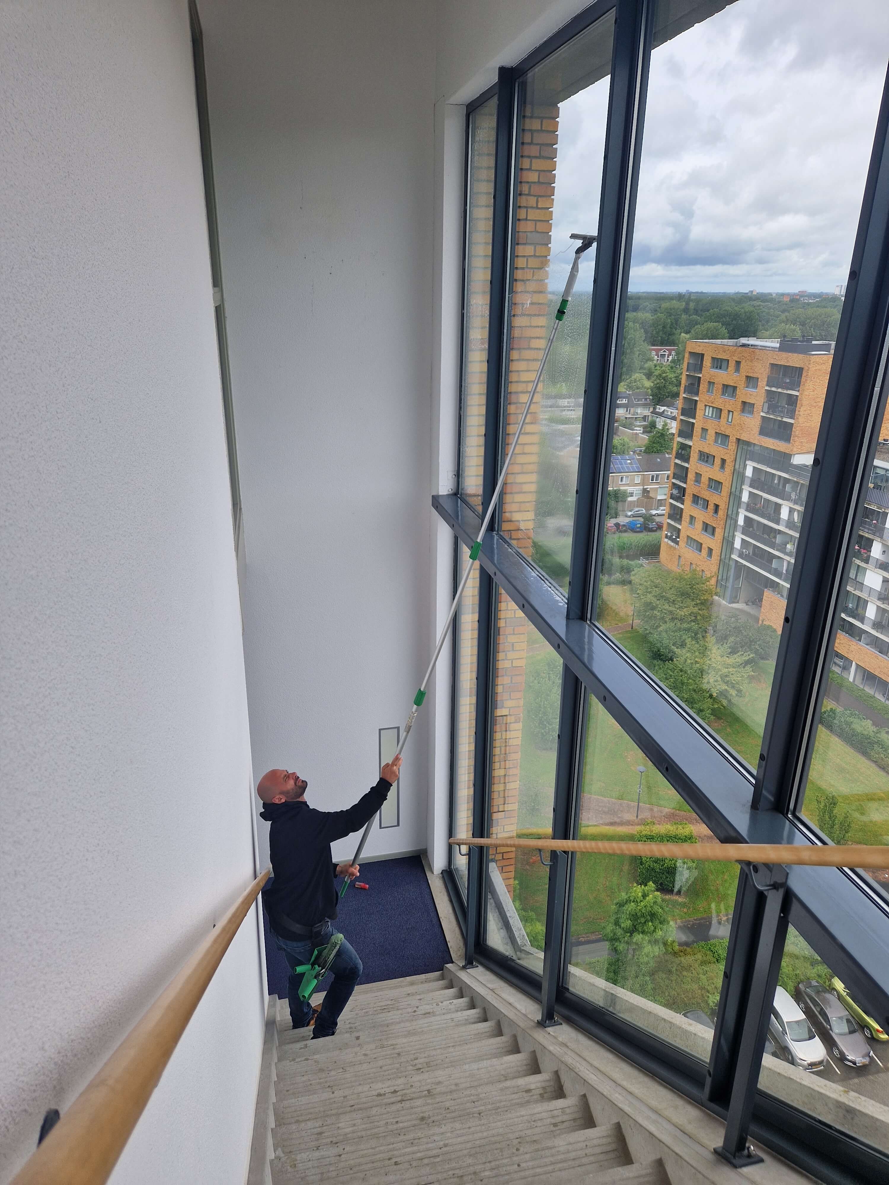 Van Klaveren reinigt het glas met een verlengsteel in het trappenhuis van een VvE aan de Fluiterlaan in Capelle aan den IJssel.