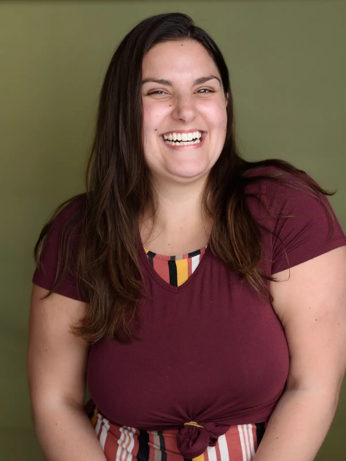 Amanda laughing, head tilted, in a deep red top against a plain wall