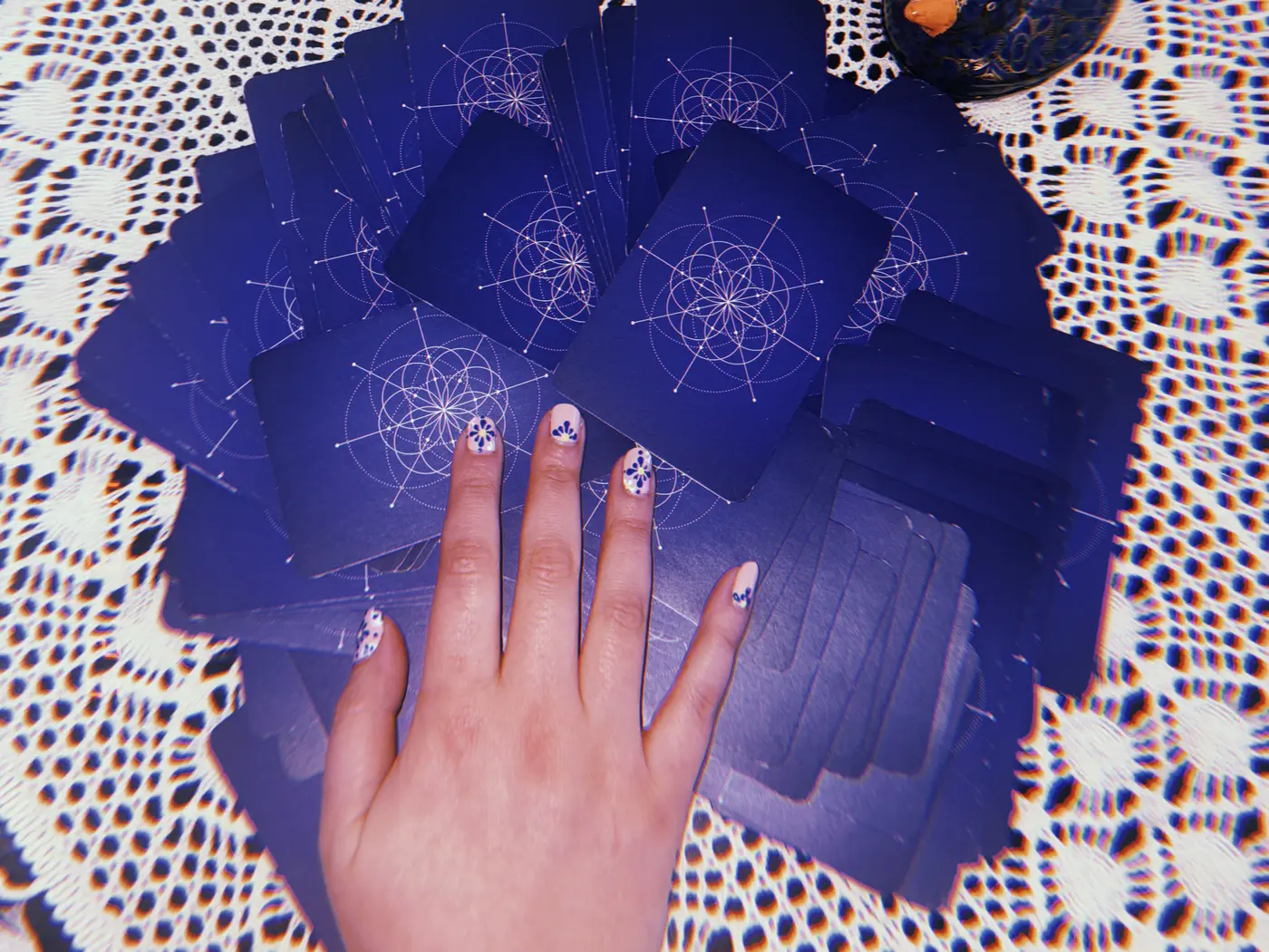 Amanda's hand resting on a fan of deep blue cards on a lace cloth, a brass eye and a stone beside them