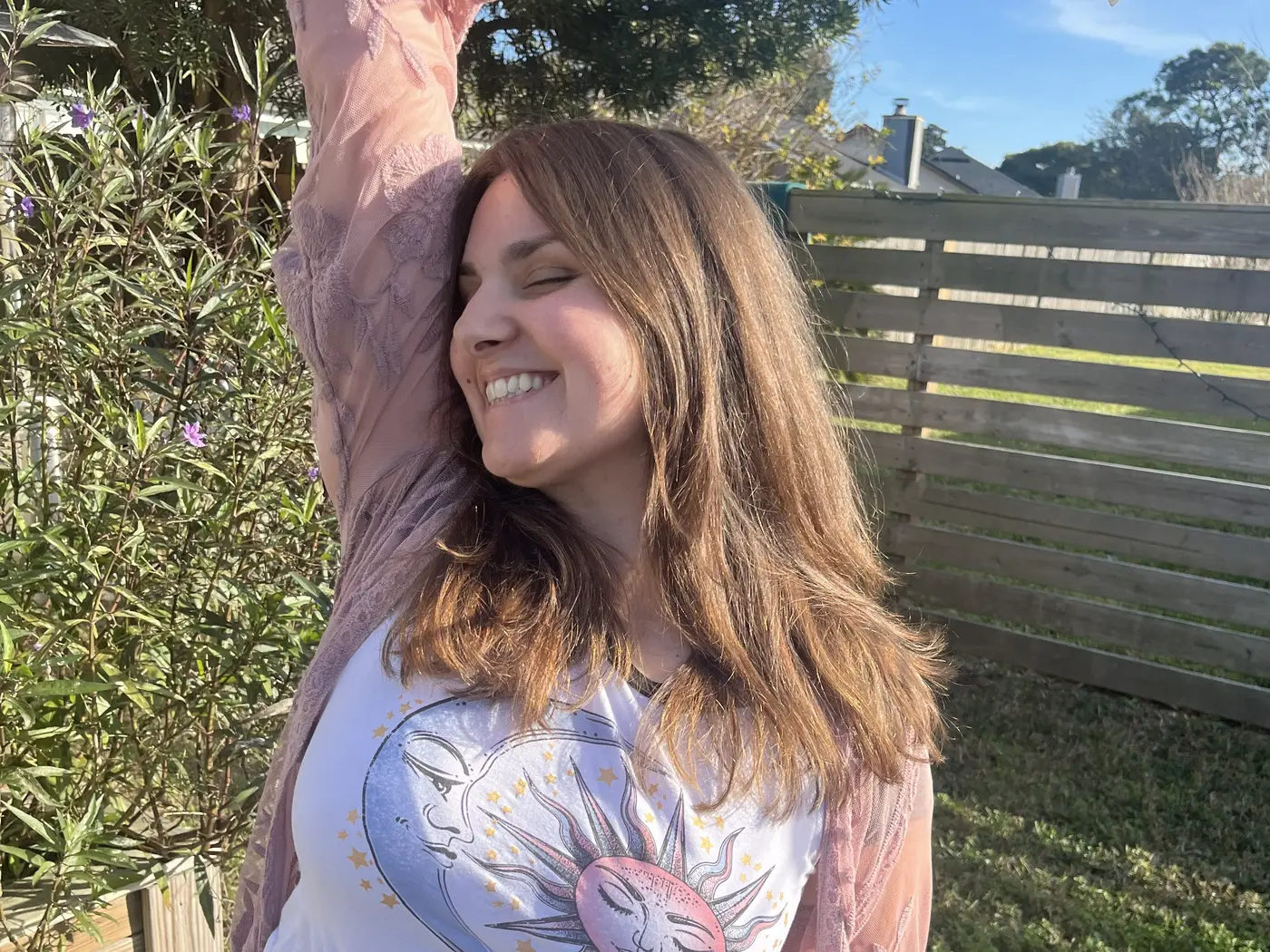 Amanda outdoors in sunlight, eyes closed and smiling, one arm stretched overhead